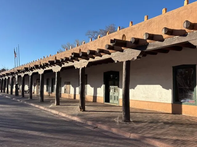 A long, traditional adobe structure with a shaded portico supported by wooden posts.