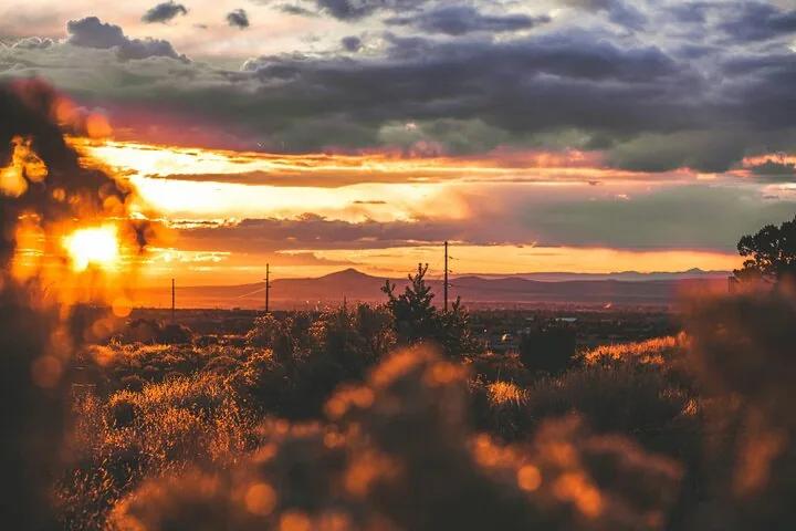 Ein leuchtender Sonnenuntergang über einer Landschaft mit fernen Bergen und niedriger Vegetation.