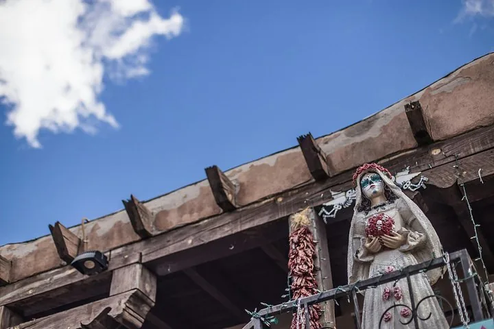 Eine Tag-der-Toten-Statue steht auf einem Balkon unter blauem Himmel.