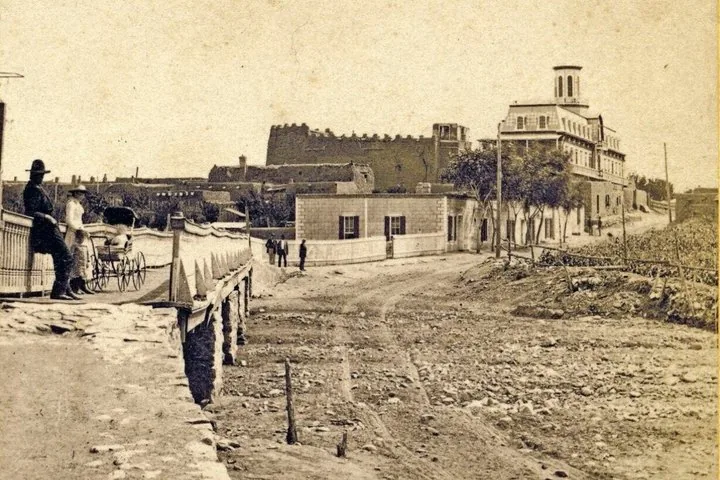 Photo vintage sépia montrant un chemin de terre, des personnes et de vieux bâtiments dans une ville.